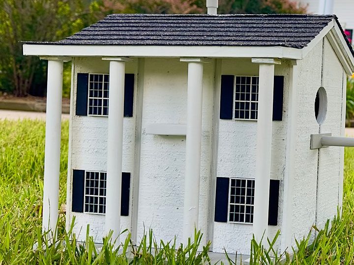 Columned house birdhouse with black shutters sitting on the lawn