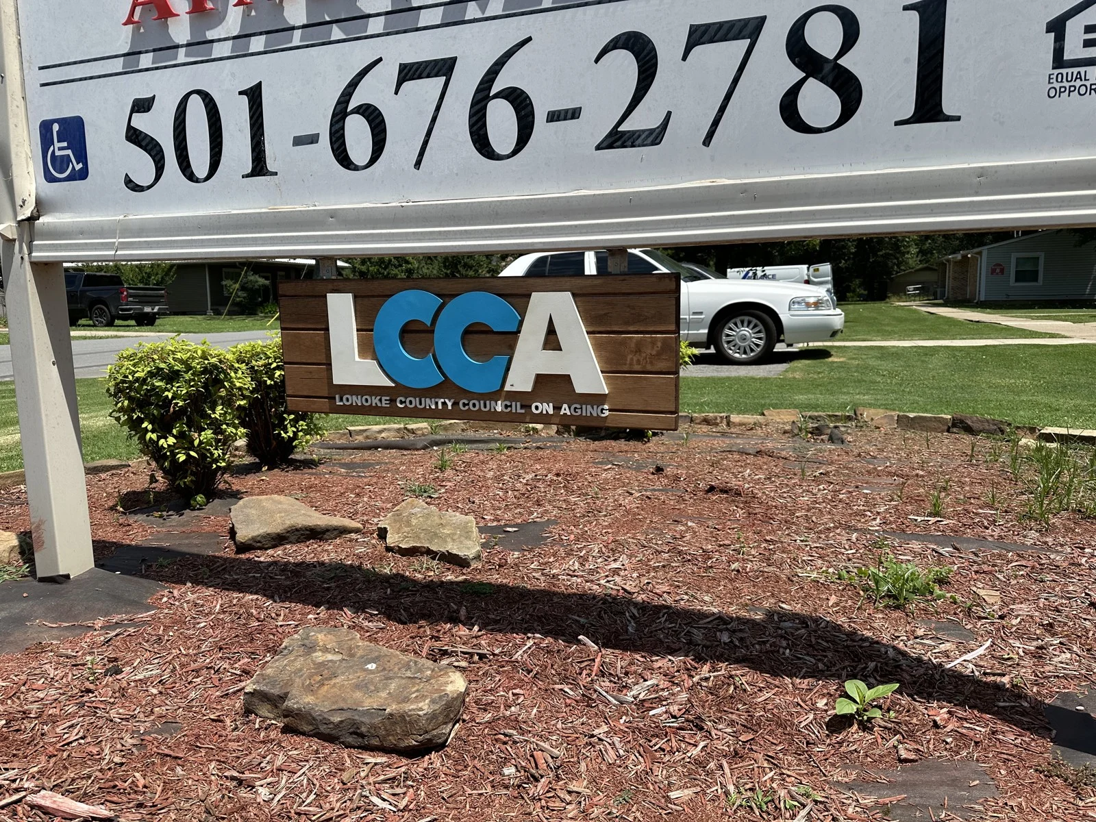 LCCA wood sign displayed beneath a larger roadside sign