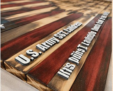 Angled view of a burned-wood flag with an engraved name and motto on the stripes