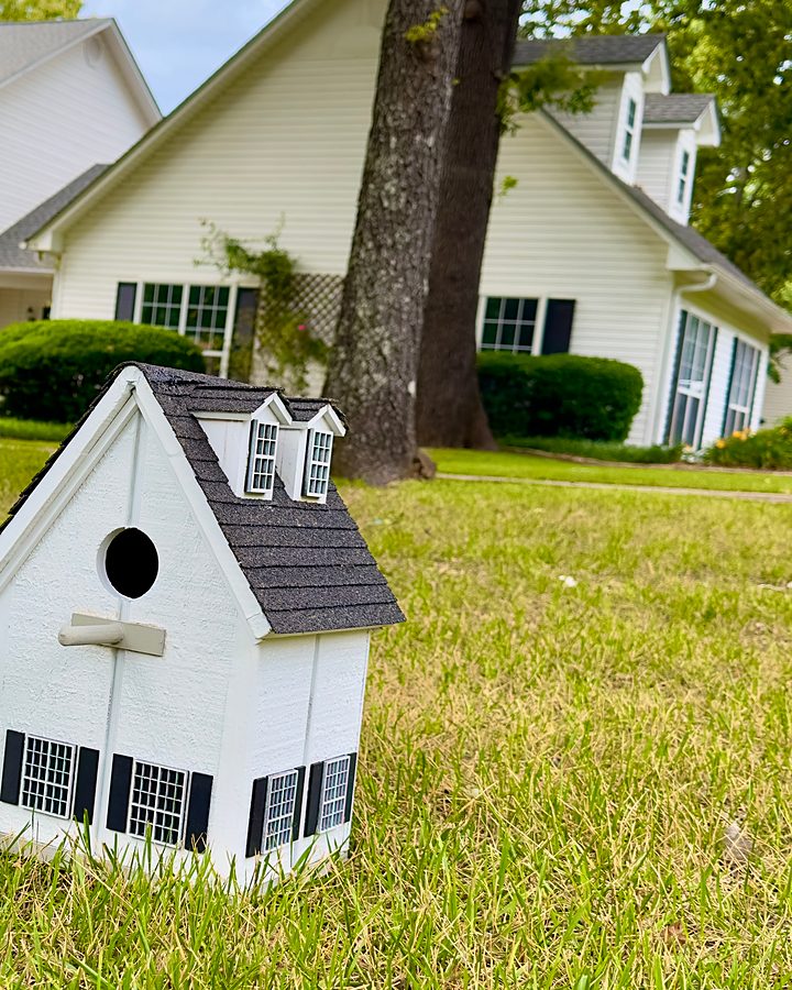 Cottage birdhouse on the lawn in front of the matching dormered home